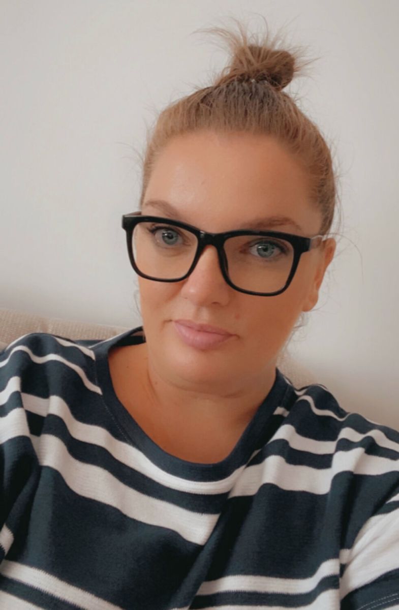 Feature image A woman in glasses and a striped shirt, standing against a neutral background with a friendly expression.