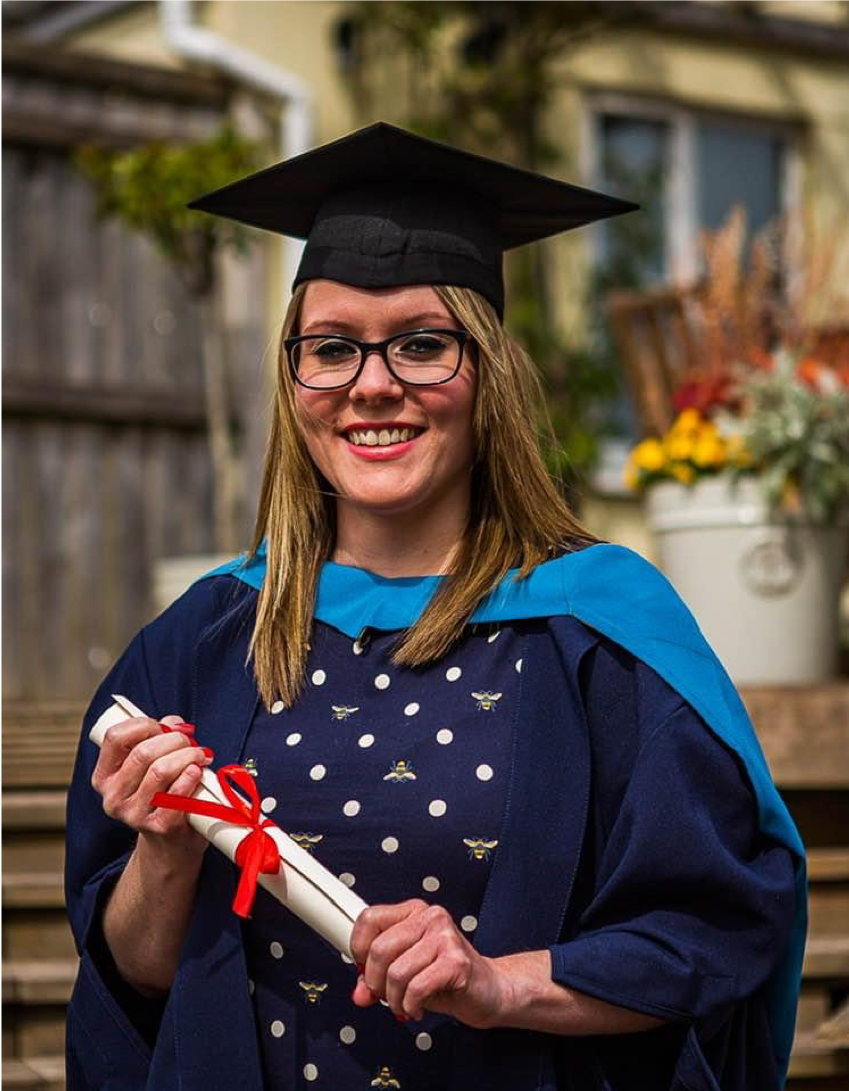 Feature image A woman in a graduation gown proudly holds her diploma, celebrating her academic achievement