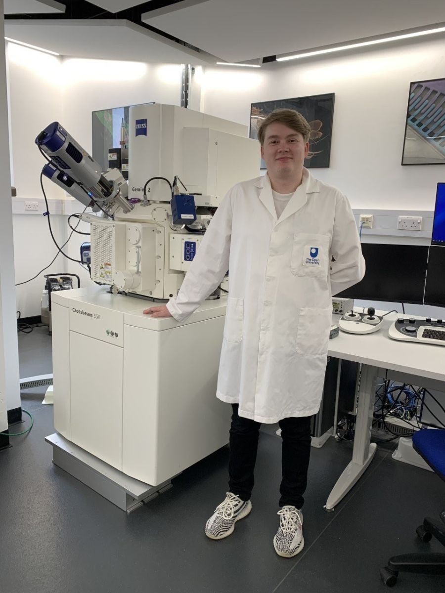 A man in a lab coat stands beside a machine, indicating a scientific or technical environment.