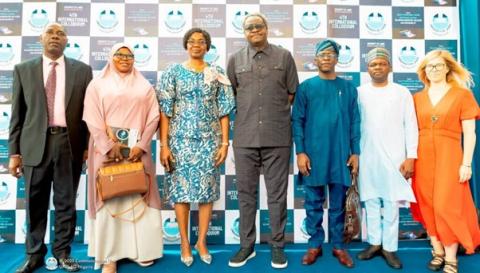 A group of people standing together on a blue carpet, smiling and dressed in formal attire