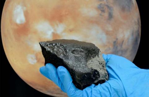 A hand holds a rock in front of a distant planet, symbolizing the connection between Earth and the cosmos.