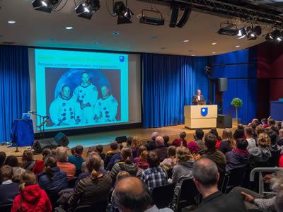 A large audience attentively watches a presentation in a well-lit conference room.