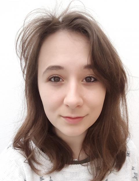 A young woman with brown hair wearing a white sweater, smiling softly at the camera.
