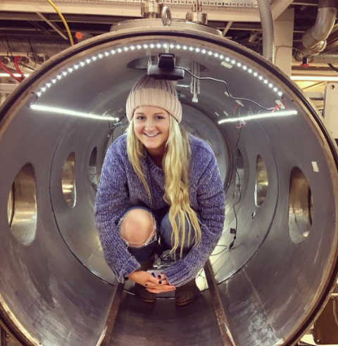 A smiling woman inside a large metal tube, conveying a sense of joy and adventure.