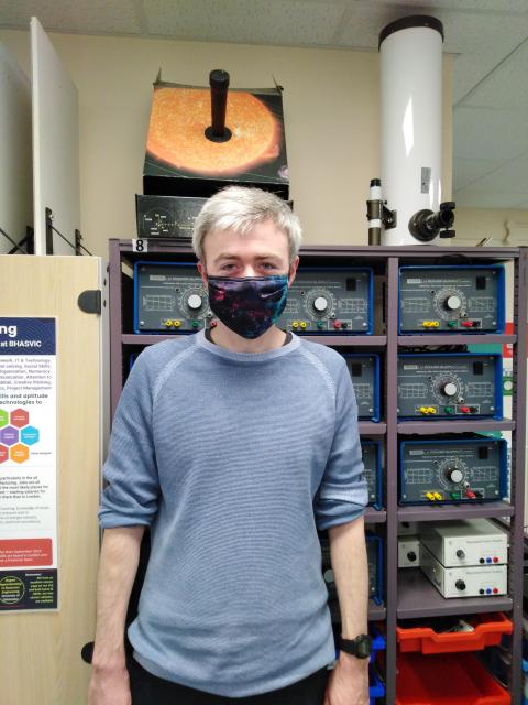 A man wearing a face mask sits in front of a computer, focused on his work or online activity.
