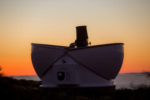 A telescope silhouetted against a vibrant sunset on a hilltop, casting a serene atmosphere over the landscape