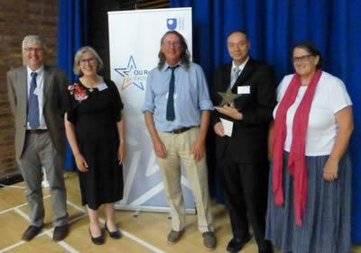 A group of people standing together, proudly holding an award, smiling and celebrating their achievement.